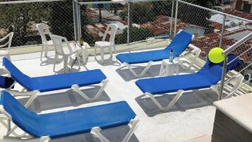 Terraza en la azotea con sillones azules y una pequeña mesa, rodeada por una cerca de malla metálica.