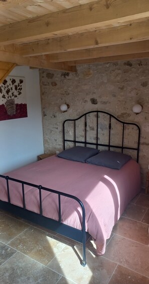 A single bed with a metal frame and a pink bedspread in a room with stone walls and a wooden ceiling. - Les Egadillias Country gite.  (Marsanne)
