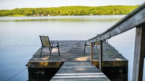 A wooden dock with two chairs facing a calm lake and a forested hill in the background. - Lakefront Peninsula Retreat w/Private Dock, on Cobbosseecontee Lake, 4 BR (West Gardiner)