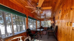 A cabin interior with wooden walls, a ceiling fan, a dining table with chairs, a sofa, and large windows with a snowy view. - Lakefront Peninsula Retreat w/Private Dock, on Cobbosseecontee Lake, 4 BR (West Gardiner)