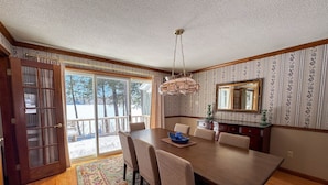A dining room with a large table, chairs, a chandelier, and a view through a glass door. - Lakefront Peninsula Retreat w/Private Dock, on Cobbosseecontee Lake, 4 BR (West Gardiner)