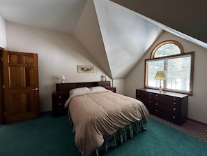 A bedroom with a sloped ceiling, a bed with a floral bedspread, a dresser with a lamp, and a window with blinds. - Lakefront Peninsula Retreat w/Private Dock, on Cobbosseecontee Lake, 4 BR (West Gardiner)
