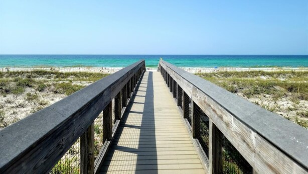 Een houten looppad naar een strand met helder turquoise water.
