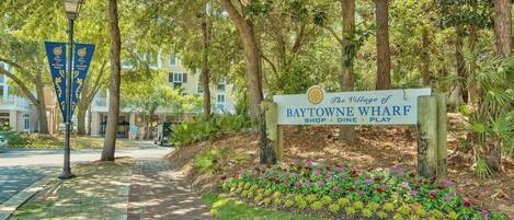A sign for The Village of Baytowne Wharf with a pathway leading to a building.
