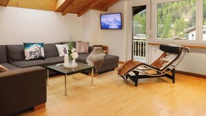 Un salon comprenant un canapé, une table basse en verre, un fauteuil inclinable en cuir et un téléviseur fixé au mur.