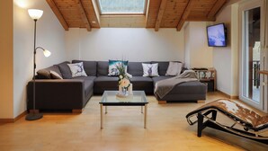 Un salon comprenant un canapé d’angle, une table basse en verre, un lampadaire, un téléviseur et une vue à travers une lucarne.