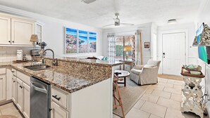 A kitchen with granite countertops, white cabinets, and a dishwasher. There is a dining area with a table and chairs, and a window with curtains. - ☀️Walk to Beach | 30A | Casa Azule- Blue Mountain Beach☀️ (Santa Rosa Beach)