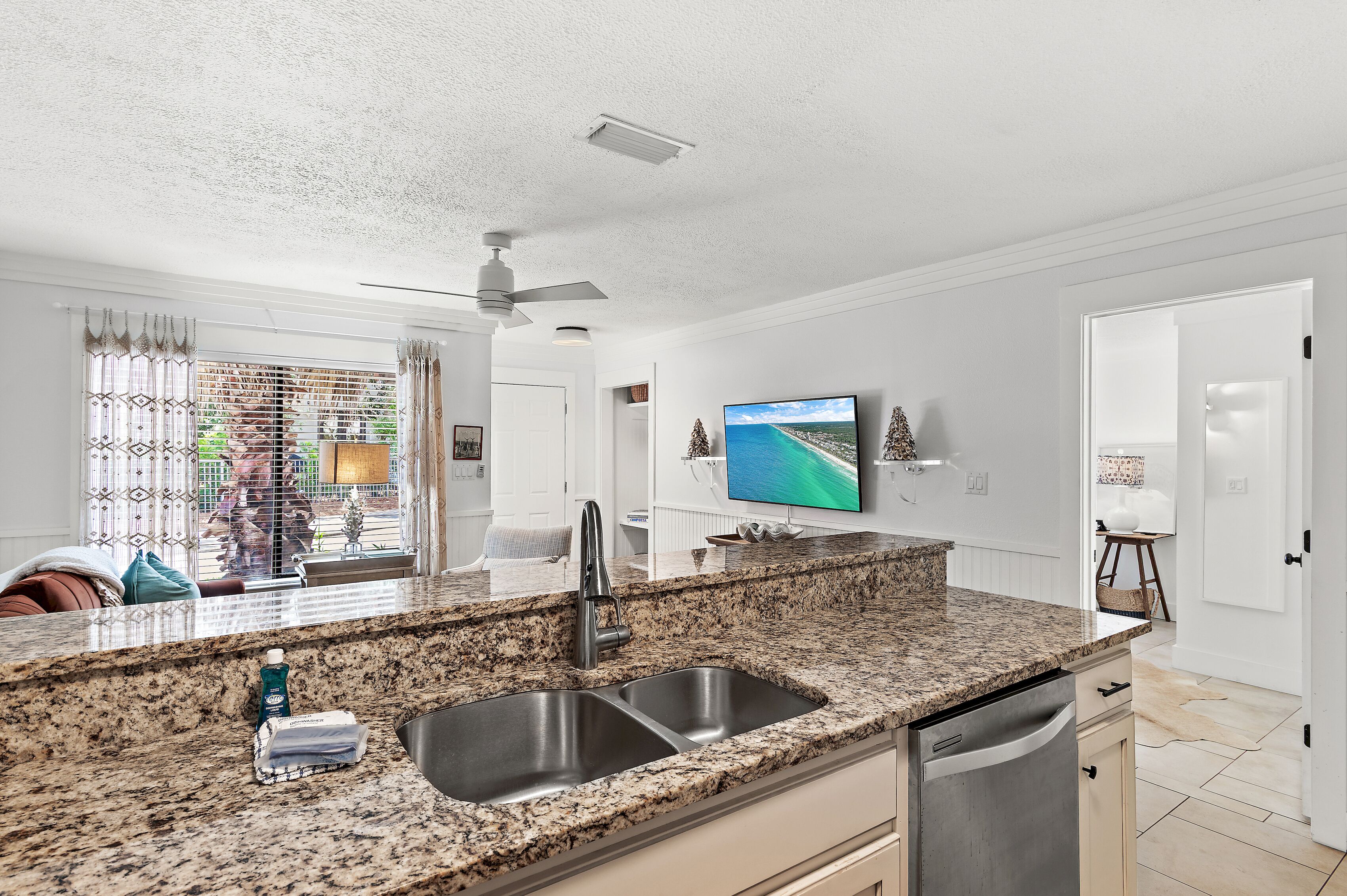 A modern kitchen with granite countertops, a double sink, and a ceiling fan.