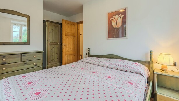 Ein Schlafzimmer mit einem Bett, einem Holzschrank, einer Tür, einem Wandbild und einer Nachttischlampe.