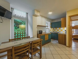 Eine kompakte Küche mit Essbereich, einem an der Wand befestigten Fernseher und einem Fenster mit Blick auf Grünflächen.