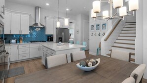 A modern kitchen with white cabinets, a blue backsplash, stainless steel appliances, and a central island. - ☀️Walk to Beach | 4 Bikes | Game Room | Emerald Escape 30A🏖 (Santa Rosa Beach)