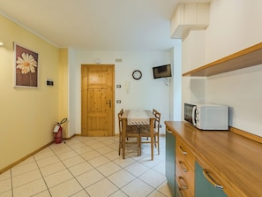 Une petite cuisine avec une table en bois, des chaises, un four à micro-ondes, une horloge et un extincteur.