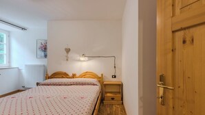Ein Schlafzimmer mit einem hölzernen Bett, einem Nachttisch, einer Wandlampe, einer Heizung und einer Holztür.
