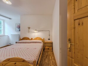 A bedroom with a wooden bed, a bedside table, a nightstand, a wall-mounted lamp, a radiator, and a wooden door. - Betulla by Interhome (Malè)