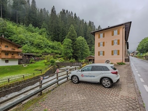 A white car parked on a cobblestone path, a building with a sloped roof, and a forested hillside in the background. - Betulla by Interhome (Malè)