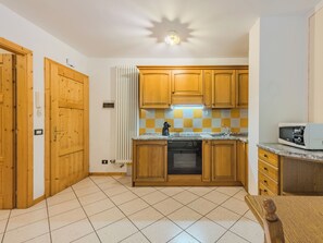 Une cuisine avec des meubles de rangement en bois, un carrelage au sol, un four encastré et un four à micro-ondes.