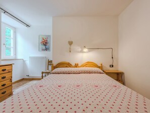 Une chambre à coucher comprenant un lit, une commode, un radiateur, une fenêtre et un luminaire fixé au mur.