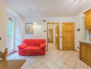 A room with a red sofa, wooden doors, and a tiled floor. - Betulla by Interhome (Malè)