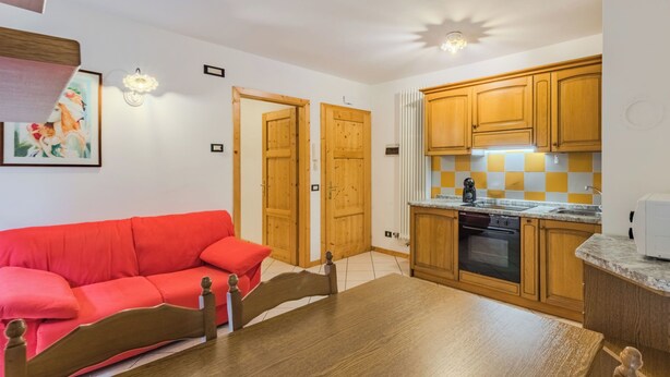 Ein kompakter Wohnbereich mit Küchenzeile, einem Holzesstisch, einem roten Sofa und Holztüren.