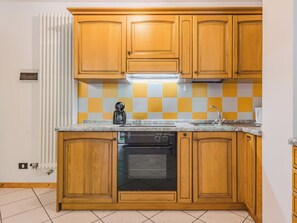 A kitchen with wooden cabinets, a built-in oven, a dishwasher, and a checkered backsplash. - Betulla by Interhome (Malè)