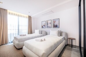 Ein Hotelzimmer mit zwei Betten, einem kleinen Nachttisch und einem großen Fenster mit Vorhängen.
