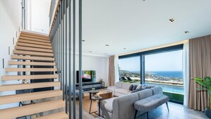 A modern living room with a staircase, a large TV, a sofa, and a view of the ocean. - Bovilla Hotel Sentio Yalıkavak (Bodrum)