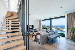 Ein modernes Wohnzimmer mit Treppe, einem großen Fernseher, einer Couch und Meerblick.