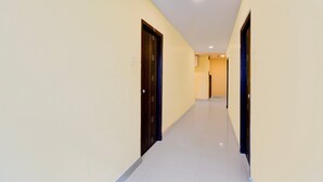 Un couloir avec des portes de chaque côté, un sol carrelé et des luminaires encastrés au plafond.