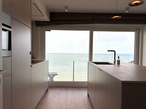Eine moderne Küche mit einem großen Fenster mit Meerblick, einer integrierten Sitzbank und einem minimalistischen Design.