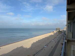Ein Strand mit einer Promenade, einem markanten Gebäude und dem Meer.