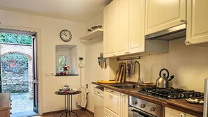 Una cucina con mobili bianchi, un fornello a gas, un forno e un piccolo tavolo con un bollitore.