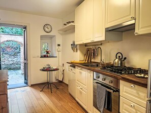 A kitchen with white cabinets, a gas stove, an oven, and a small table with a kettle. - Bellissimi e Paola by Interhome (Dolcedo)