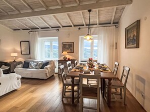A cozy room with a wooden dining table set for four, a sofa, a lamp, and a view of the outdoors through large windows. - Bellissimi e Paola by Interhome (Dolcedo)