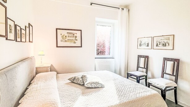Una camera da letto con un letto, una sedia, un comodino e quadri appesi al muro.