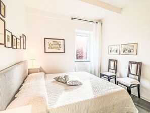 Ein Schlafzimmer mit einem Bett, einem Sessel, einem Nachttisch und gerahmten Bildern an der Wand.