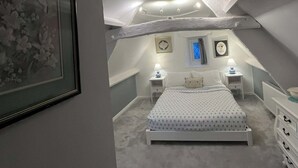 Un dormitorio con techo inclinado, una cama, mesitas de noche, un aparador y cuadros enmarcados.