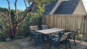 Un patio con una mesa y sillas de madera, un camino de piedra y una valla de madera.