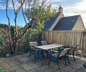 A patio with a wooden table and chairs, a stone pathway, and a wooden fence. - Charming Cotswold cottage with stunning views. (Stroud)