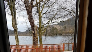 A view through a doorway of a gravel area with a wooden fence, trees, and a body of water in the background. - House on the shores of Loch Shiel in Historic Glenfinnan, Monument and Viaduct (Glenfinnan)