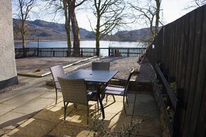 Un patio al aire libre con mesa y sillas, una cerca de madera y vistas a un lago y colinas.