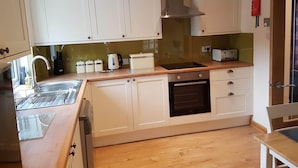 A compact kitchen with white cabinets, a stainless steel range hood, a built-in oven, and a toaster. - House on the shores of Loch Shiel in Historic Glenfinnan, Monument and Viaduct (Glenfinnan)