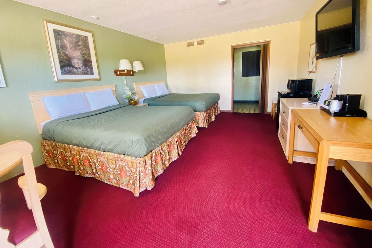 A hotel room with two beds, a desk, a television, and a door leading to another room.