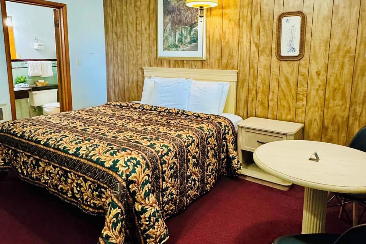 A hotel room with a bed, bedside table, chair, and a small table.