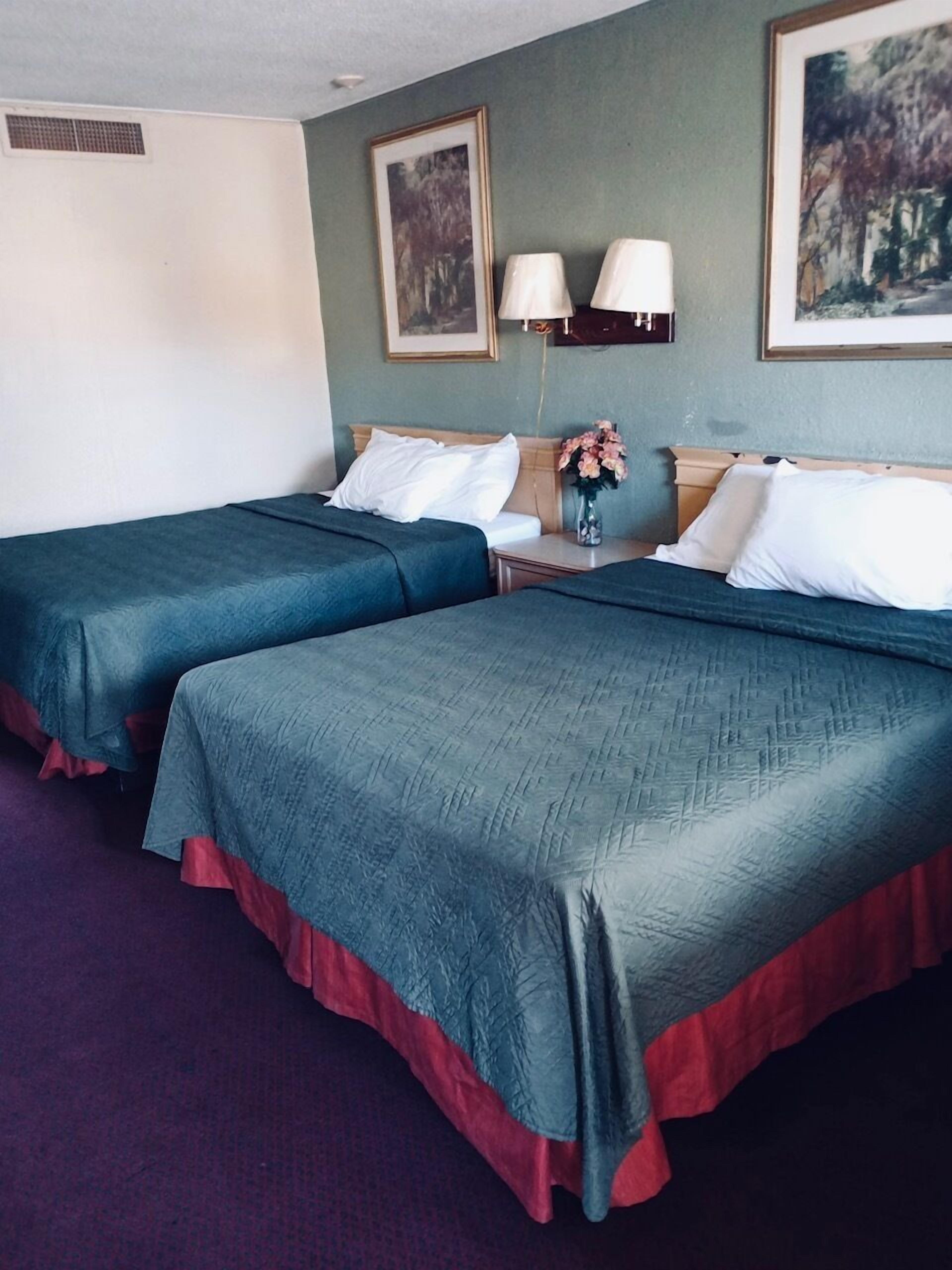 A hotel room with two beds, a nightstand with lamps, a vase with flowers, and framed pictures on the wall.