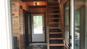 A wooden interior with a staircase, a door leading outside, and a small rug on the floor. - Mohican Cabin Private Getaway (Perrysville)