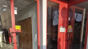 Entrada d'un edifici amb portes de vidre, un marc vermell i un senyal de precaució.