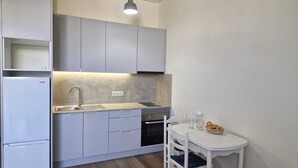 Cuina compacta amb forn integrat, un rentaplat i zona menjador amb taula i cadires petites.