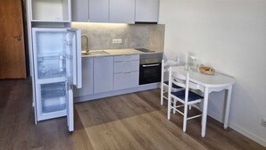 Cuina compacta amb frigorífic integrat, fogó i un rentamans. Hi ha una taula de dinar petita amb caires.