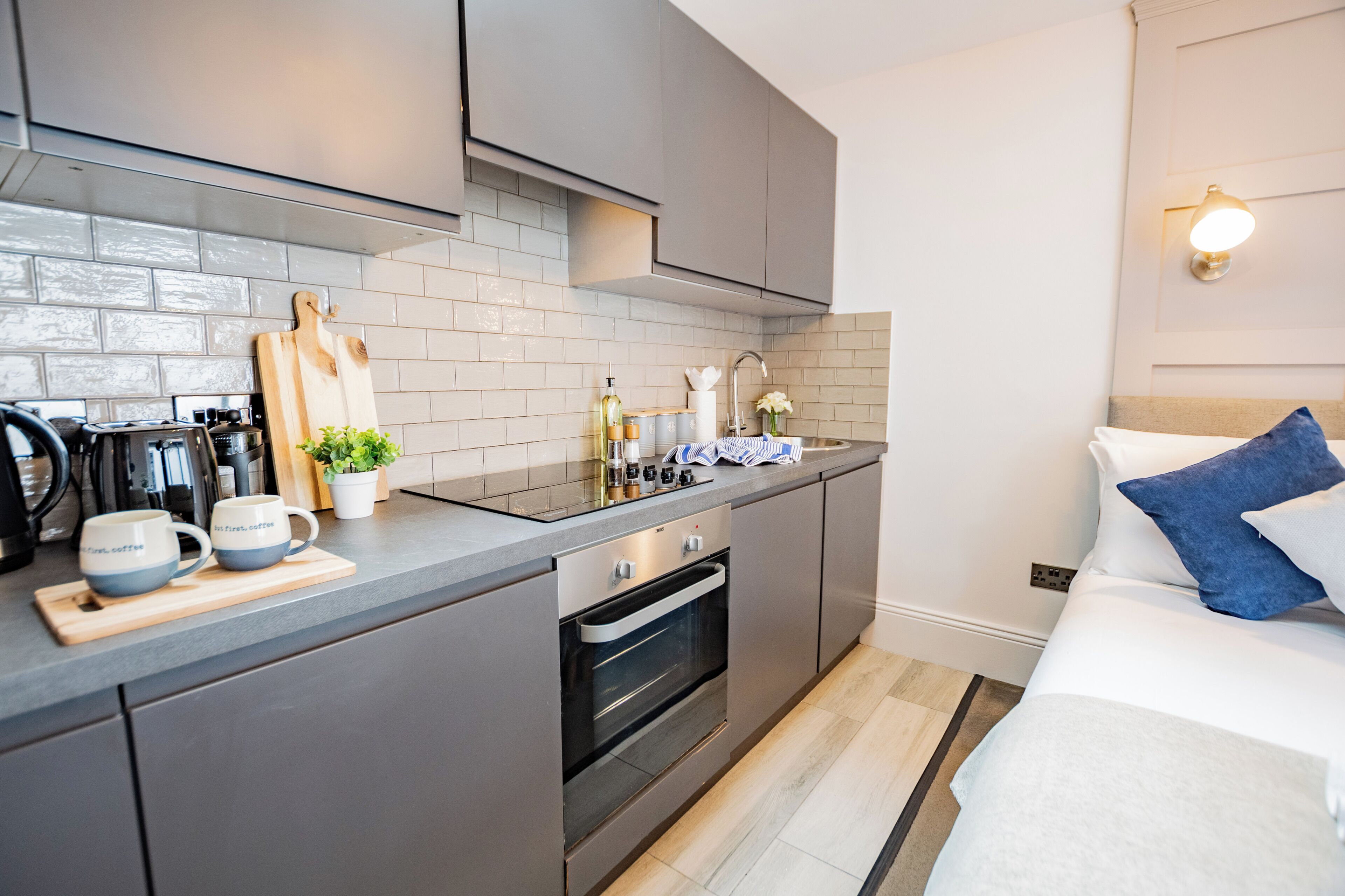 A modern kitchen with grey cabinets, a built-in oven, and a countertop with coffee mugs and a cutting board.