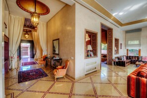 Eine großzügige Lobby mit hoher Decke, gemusterten Bodenfliesen, einer Sitzecke mit Sofas und einem Essbereich.